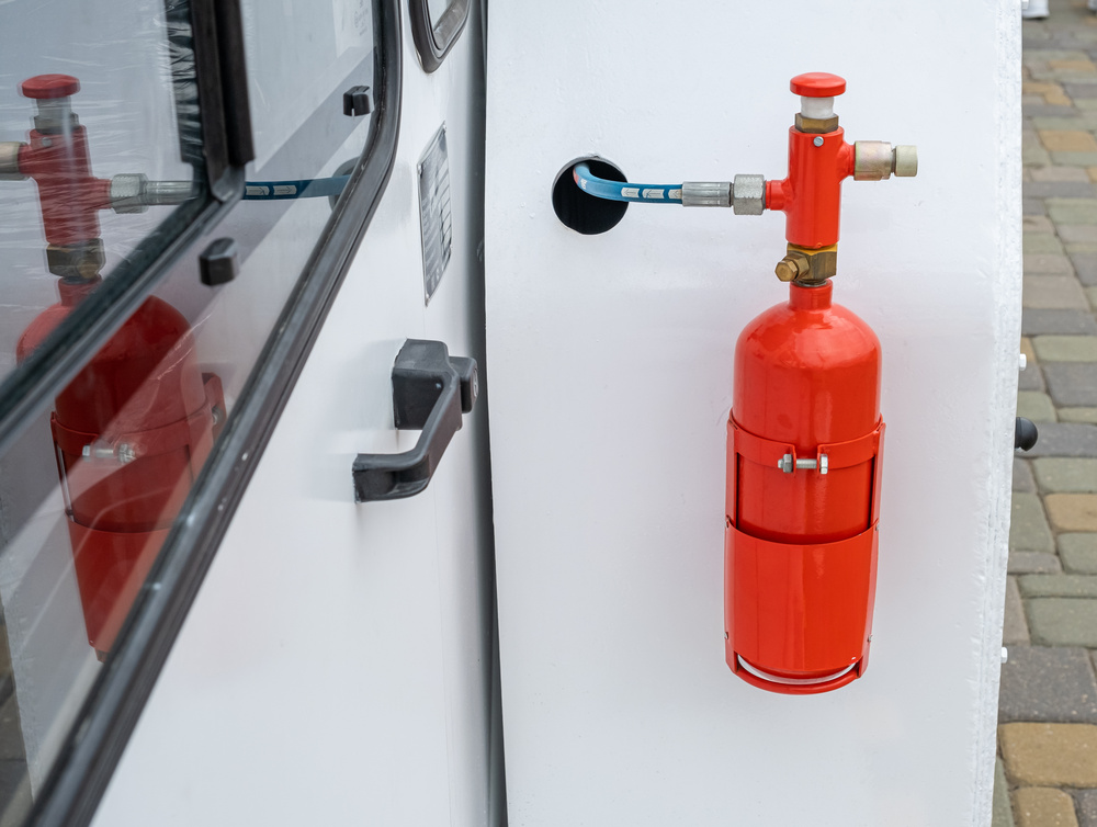 Close-up of a red fire extinguisher cylinder mounted on a white industrial vehicle. Fire safety equipment and suppression system on a professional truck or machinery for emergency response